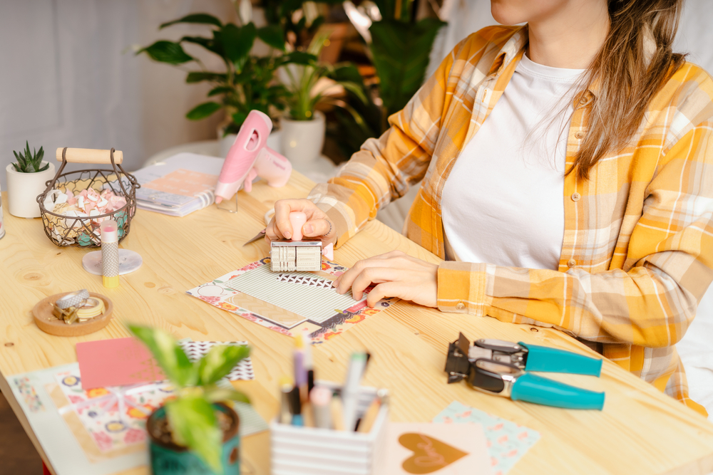 Plan recadré de femmes réalisant un album de scrapbooking DIY à l'aide d'un pistolet à colle, d'une agrafeuse et de papier de scrapbooking à motifs.